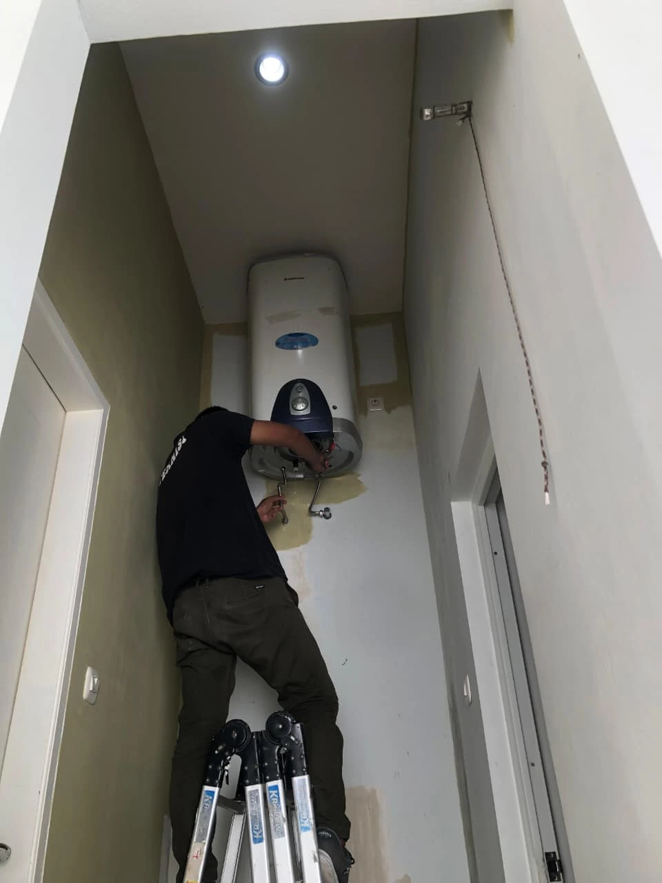 Teknisi sedang memeriksa heating element water heater di rumah mewah Medan Johor, dinding putih bersih dan penerangan terang
